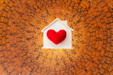Red heart on wooden house model over blurred Feng Shui compass plate background, buy new house, real estate business