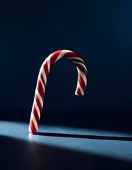 Fotobehang A single candy cane forming a graceful arch, its red and white stripes popping against a deep navy backdrop © patsai