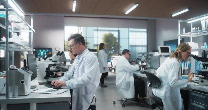 Establishing Footage of a Group of Scientists in White Lab Coats Walking in Workplace, Sitting Behind Desks and Using Computers. Young Creative People Working in a Research Laboratory