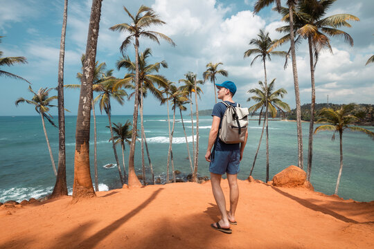 Traveler with backpack walking among coconut palm trees on hill aagainst tropical beach in Sri Lanka. .