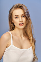 A young blonde woman in a white top striking a pose in a studio setting, exuding elegance and grace.