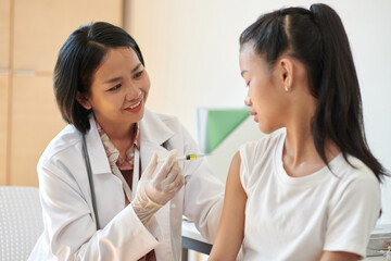 Smiling doctor injecting vaccine in arm of teenage girl