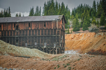 Fototapeta na wymiar Majestic old mining building paired with pine trees and a rugged excavation site in Colorado, showcasing the raw nature and mountainous terrain of the heart land