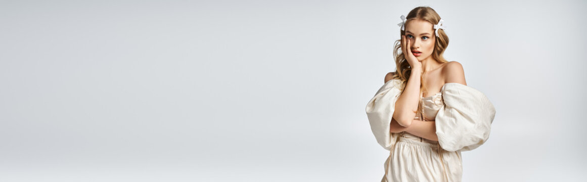 A young, blonde woman exudes elegance in a white dress while posing in a studio setting.
