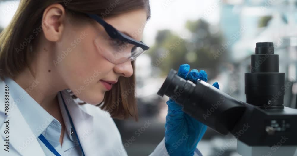 Aufkleber close up portrait of a female microbiologist wearing safety glasses and looking through the microsco