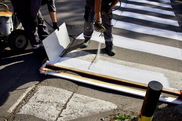 A worker applies paint from a spray gun to the asphalt, painting a pedestrian crossing, renewing...