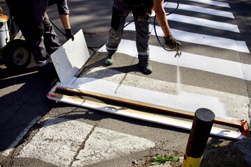 people draw markings for a pedestrian crossing on the asphalt using a spray gun and a wooden...