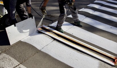 workers using a spray gun apply markings to the asphalt