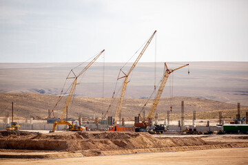 Lifting cranes and other equipment at a construction site. A group of lifting platforms for construction and loading and unloading operations. Construction at the initial stage.