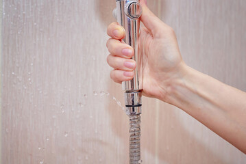 Laaking water hose close to shower head, water flow from the hole of the hose closeup. Broken shower hose, bathroom leaks, common water issues in home. Hand holding leaky hose.