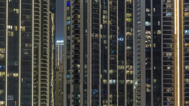 Tall blocks of flats with glowing windows located in residential district of city aerial timelapse. Evening light in rooms of apartments in towers and illuminated skyscrapers