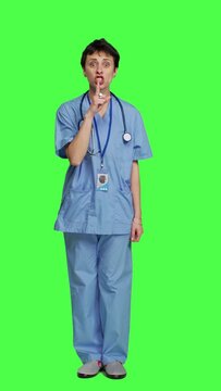 Front view Medical assistant asking to keep quiet and be silent against greenscreen, showing hush mute symbol to keep privacy and silence. Young nurse showing secrecy taboo sign. Camera A.