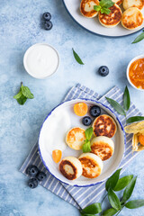 Cheese pancakes, fritters or syrniki with blueberry, physalis and yogurt, blue background. Healthy and tasty breakfast.