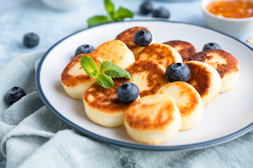 Cheese pancakes, fritters or syrniki with blueberry, physalis and yogurt, blue background. Healthy and tasty breakfast.