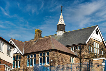 Traditional brick school building with a spire against a blue sky with wispy clouds in Harrogate,...