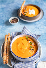 Bright vegetarian autumn pumpkin and carrot soup with seeds, mint and spices, blue background. Comfort food, fall and winter healthy slow food concept.