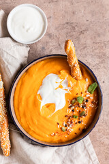 Pumpkin and carrot soup with cream, mint and seeds on brown concrete background. Traditional autumn or winter vegetarian soup with creamy silky texture.
