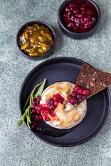 Baked camembert cheese on plate with cranberry sauce, orange jam, toasted bread with seeds and rosemary. Brie type of cheese. Italian, French cheese.