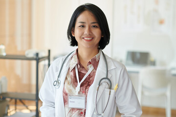 Portrait of smiling general practitioner in white coat standing in her office