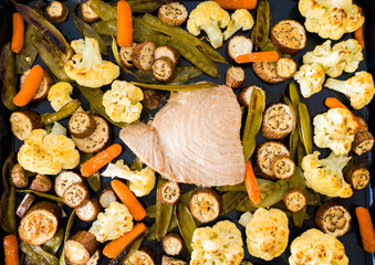 Baked tuna fillet on a baking sheet with baked vegetables. Healthy food background.