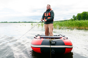 A man's hobby. A fisherman in a safety vest catches fish standing in a boat