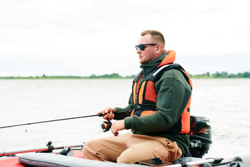A fisherman with a spinning rod is sitting in a boat. Men's hobby