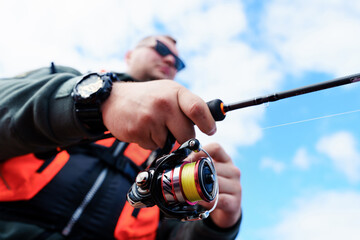 Close-up of a reel with a spinning line in the hands of a fisherman outside. Summer fishing