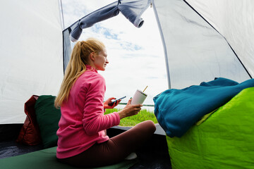 A young woman is sitting in a tent and taking nature photos on her smartphone. Summer holidays