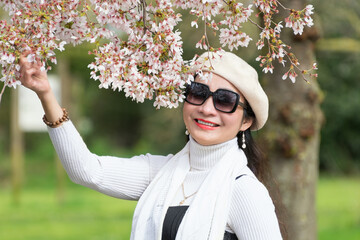 Portrait of a beautiful young Vietnamese woman against the background of cherry blossoms, sakura in pastel colors, who holds a sakura branch with her hand. Spring concept.
