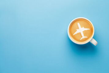 Draufsicht, Weiße Tasse mit Kaffe und Flugzeug Latte Art im Milchschaum isoliert auf blauem Hintergrund - Konzept für entspanntes Reisen, Reiselust - obrazy, fototapety, plakaty