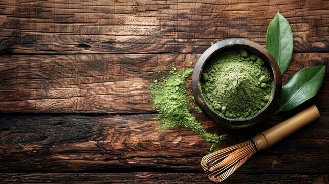 organic matcha green tea powder in bowl with wire whisk and green tea leaf on wooden background
