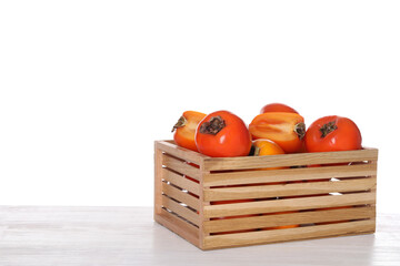 Delicious ripe juicy persimmons in crate on wooden table against white background
