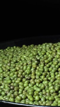 Close-up of organic natural dried green mung beans (Vigna radiata) rotating on a plate. Green gram or maash beans with black copy space. Concept of healthy lifestyle, vegetarian or vegan food diet.