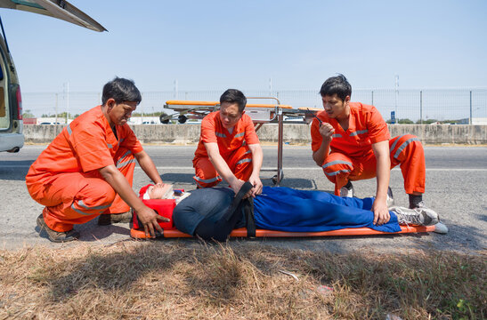 Three paramedics practice first aid beside an ambulance on a sunny day. Urgent assistance during road accident.
