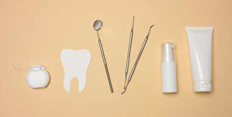 Dental mirror, tube of toothpaste and dental floss on a brown background