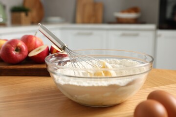 Cooking process. Metal whisk, bowl, flour, eggs and apple on wooden table in kitchen, closeup