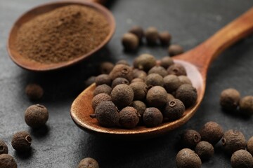 Ground and whole allspice berries (Jamaica pepper) on black table, closeup