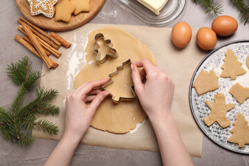 Woman making Christmas cookies with cutters at grey table, top view