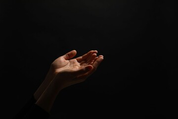 Religion. Woman with open palms praying on black background, closeup. Space for text