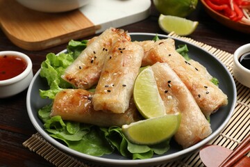 Tasty fried spring rolls, lettuce and sauce on wooden table, closeup