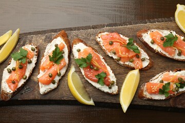 Tasty canapes with salmon, capers, lemon and cream cheese on wooden table, top view