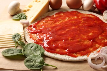 Pizza base smeared with tomato sauce and products on parchment, closeup