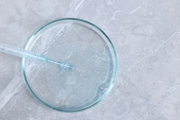 Glass pipette and petri dish with liquid on grey marble table, top view. Space for text