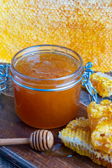 A glass jar of thick golden honey with wooden spoon and honeycombs. Concept of beekeeping, apiculture, apiary. Sweet honey product, healthy food - 780573701
