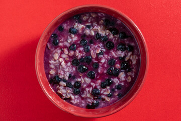 Oatmeal porridge with ripe blueberries for healthy breakfast on red background, closeup, top view - 780573745