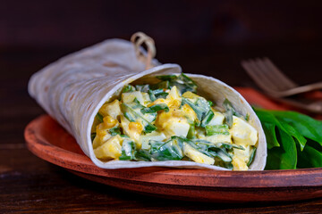 Homemade burrito wraps with boiled eggs, potato, green wild garlic and sour cream for healthy breakfast on plate, closeup - 780573771