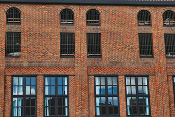 Facade of a vintage brick building with rows of windows reflecting the sky, showcasing industrial...