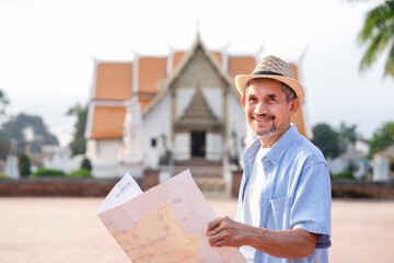 portrait happy asian senior man wears hat,holding a paper map,smiling,standing in front of temple,elderly people visiting buddha temple, travel destination in asian,Thailand