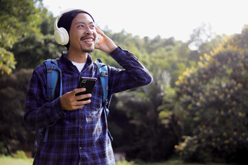 Young Asian man in a casual outfit, sporting a beanie, plaid shirt, backpack, and headphones,...