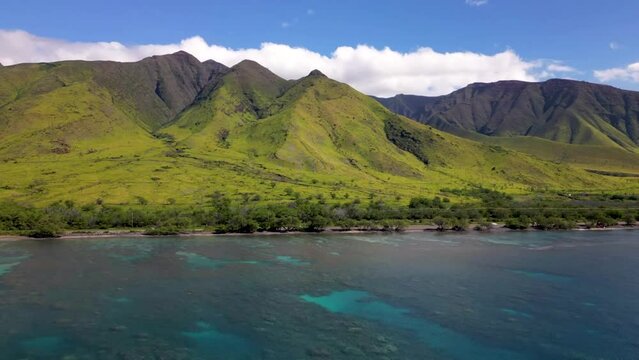 Aerial time lapse of waves crashing on beach on Maui coastline with classic Hawaii ridge mountain peaks above. 